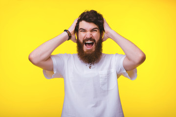 Bearded man is screaming with raised hands near his head on a yellow background.