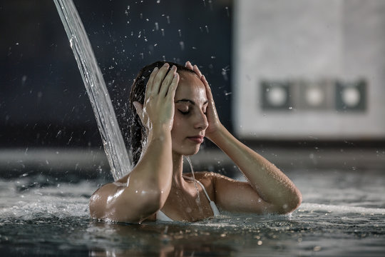 Concentrated Woman Touching Head Under Water Stream In Pool