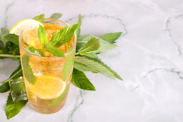 Glass of iced tea with mint and lemon on marble table. Cold drink.