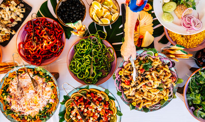 Vertical view of senior woman hand serving food on a dish from catering table during party celebration - catering and restaurant concept with mixed chef food on a table -coloured background together
