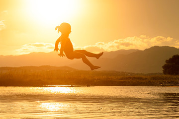 3 year old girl jumps into the sea at sunset.