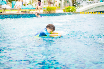 A boy is playing and swimming at the swimming pool in the evening.