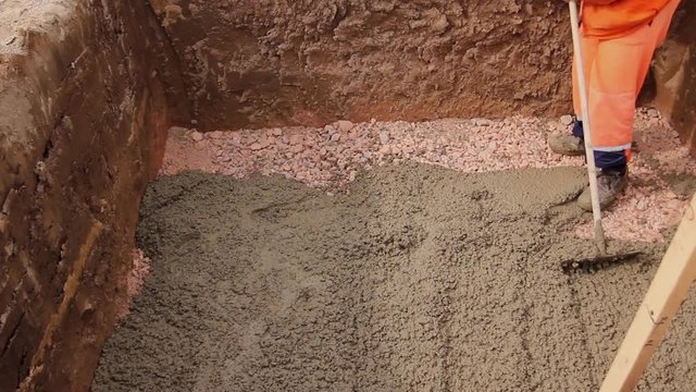 Worker is leveling concrete after pouring. Mason is using rake to spreading fresh concrete in square trench.  H.264 video codec