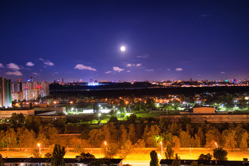 Night city panorama with urban landscape and illuminated buildings under moon and night sky. Kiev