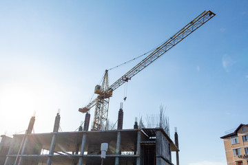 Fototapeta premium Tower crane on the blue sky background. Building construction work concept, investments in the development construction buildings and structures industry.