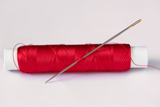 Close up image of needle and red thread on white background