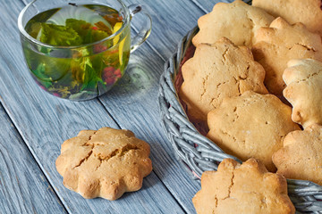 Biscuits in the wicker basket from newspaper tubules and a transparent cup of green tea with mint and red currants on blue wooden background. Closeup, selective focus