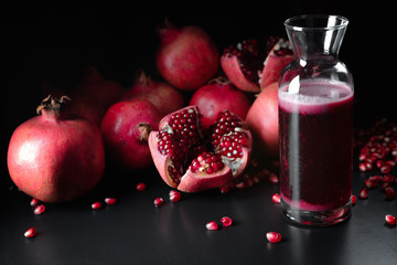 Pomegranate juice in a decanter on a background of pomegranates on a black background