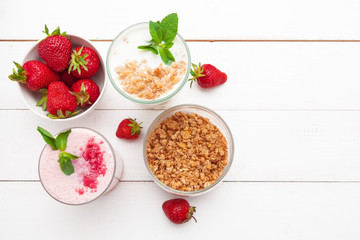 Healthy breakfast with yoghurt, granola and strawberries on white wooden background top view
