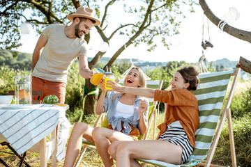 Young friends having fun, drinking juice at the beautifully decorated yard with dinner table during...