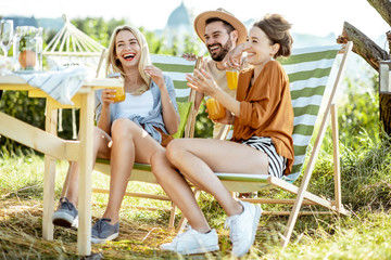 Young friends talking and having fun, while sitting together with summer drinks on the sunbeds at the backyard during the sunny day