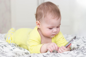 Baby girl boy playing with a smartphone. A baby in yellow 6 months holding a mobile phone