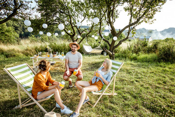 Young and cheerful friends relaxing with drinks, sitting on the sunbeds in the beautifully...