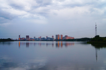 Fototapeta na wymiar The modern city center is reflected in the water of the lake. Glowing buildings in the evening.