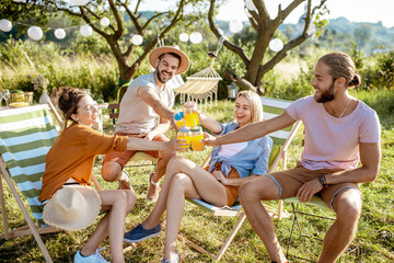 Young and cheerful friends relaxing on the sunbeds, clinking glasses in the beautifully decorated...