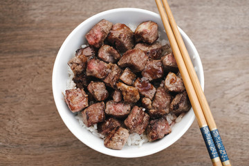 Homemade Bowl of Diced Beef Steak with rice Japanese style on wooden table.