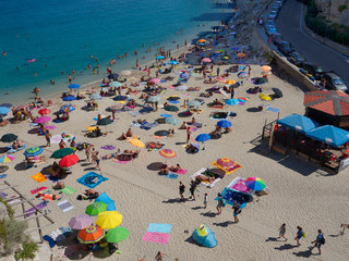 Crowded and popular beach with pale sand and blue sea, many bathers and umbrellas, Tropea, Italy