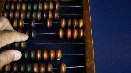 Vintage wooden abacus close up. A man s hand moves wooden knuckles on the bills. Part of the old end of the abacus on a dark blue background