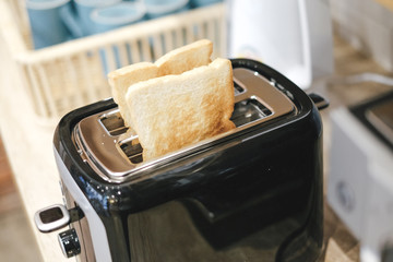 Roasted toast bread popping up of black toaster on a wooden table