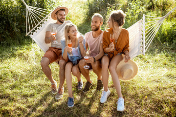 Portrait of a group of cheerful friends sitting together on the hammock, having fun outdoors during...