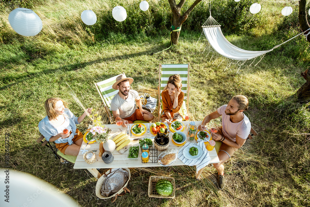 Wall mural group of a young friends having festive lunch in the beautifully decorated garden on a summer aftern