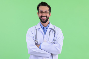 Happy young bearded Persian man doctor smiling with arms crossed