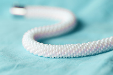 White beaded necklace on a blue textile background close up