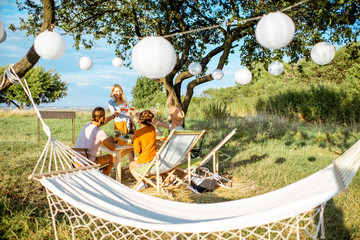 Young people having festive lunch in the beautifully decorated garden with hammock and garland on a summer afternoon
