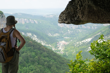 a girl-traveler in a backpack looks into the distance from a cliff on the ruins of a medieval fortified city