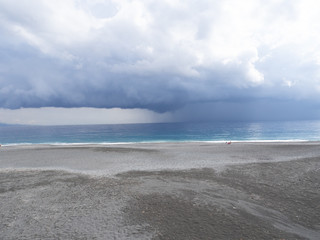 Obraz premium Distant rain and dramatic dark sky over sea with gravel beach in foreground