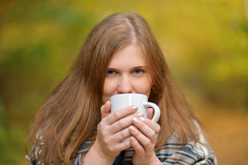 Autumn.  Cold girl. Portrait of a smiling girl with a Cup of hot tea in her hands, wrapped in a blanket in the autumn forest . Autumn background