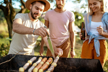Group of a young friends having barbecue, cooking food in the beautiful garden, during a festive lunch on a summer aftenoon
