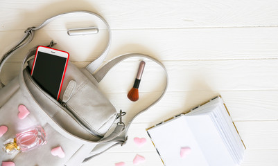 Phone, stylish bag and perfumes on white background. Beautiful flat lay. Things for business woman. Note book schedule. Makeup kit. Girl's gift with hearts.