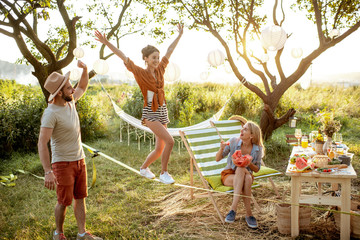 Young friends having fun, walking on a slackline during a picnic in the beautifully decorated garden on a sunset