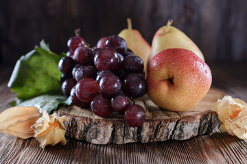 Juicy fruits such as pears and a bunch of muscat grapes beautifully lit by light on a dark background lie on a wooden table