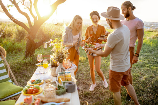 Group of a young and happy friends having fun during a festive picnic in the beautifully decorated garden with lunch table on a sunset