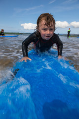 Little boy learning to surf at the beach, getting up on surfboard for the first time, west coast of...