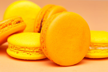 Orange and yellow macarons or macaroons stacked over pinky orange background.