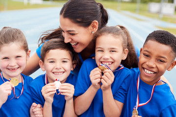 Children With Female Coach Showing Off Winners Medals On Sports Day