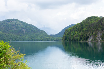 Postcard view of Alpsee Lake surrounded by Alps mountains, Bavaria, Germany. Spring summer time. Blue clear water. Noone. Copy space. Space for text. Travel and Nature concept. Nature beauty.
