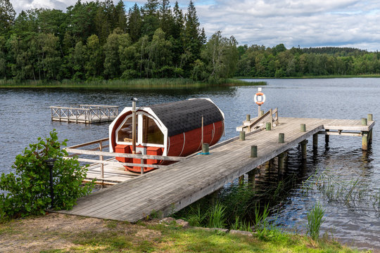 Summer lake nature landscape view of a traditional scandinavian water floating red wooden sauna spa next to a jetty.