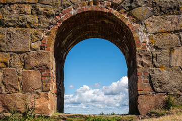 Summer view through an old medieval stone wall arched gate at Varberg Fortress in Sweden with blue cloudy sky in the background.