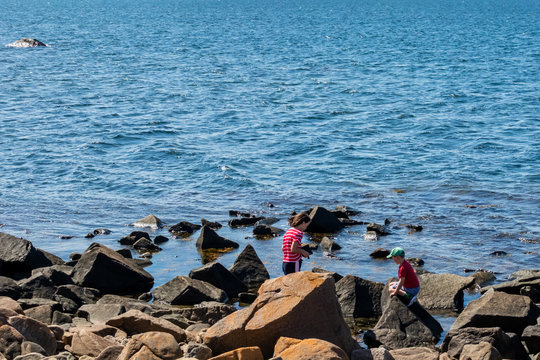 Beautiful summer seaview of two children playing on stone rocks on the shore with blue water in Varberg Sweden.