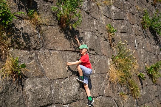 A young caucasian boy child climbing on a large massive stone wall with many green plants at Varbergs Fortress in Sweden.