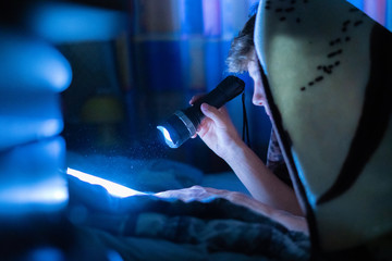 young person with a light torch reading books in bed at night in bedroom