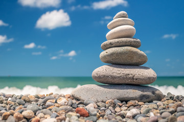 Fototapeta na wymiar pyramid of sea pebbles on the beach against the backdrop of the sea wave in sunny day. concept of balance harmony and meditation. copy space