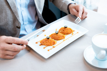 cropped view of businessman holding fork and knife while sitting at table with delicious dish