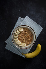 Organic healthy oatmeal porridge with fresh bananas. The white porcelain bowl with napkin underneath bowl.