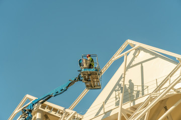 Painter, plasterer in special clothes, paint the facade of the building with white paint roller at...