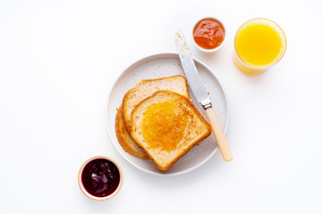 Morning toasts with butter and confiture on white table served with orange juice. Flatlay, view...